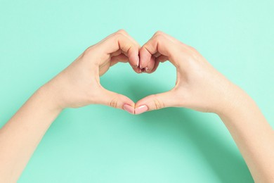 Woman showing heart gesture with hands on cyan background, closeup