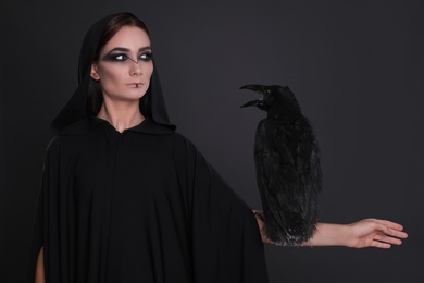 Photo of Mysterious witch with raven on black background
