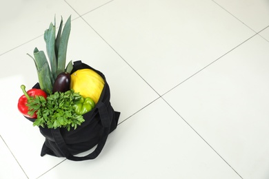 Photo of Black tote bag with vegetables and fruit on floor, above view. Space for text