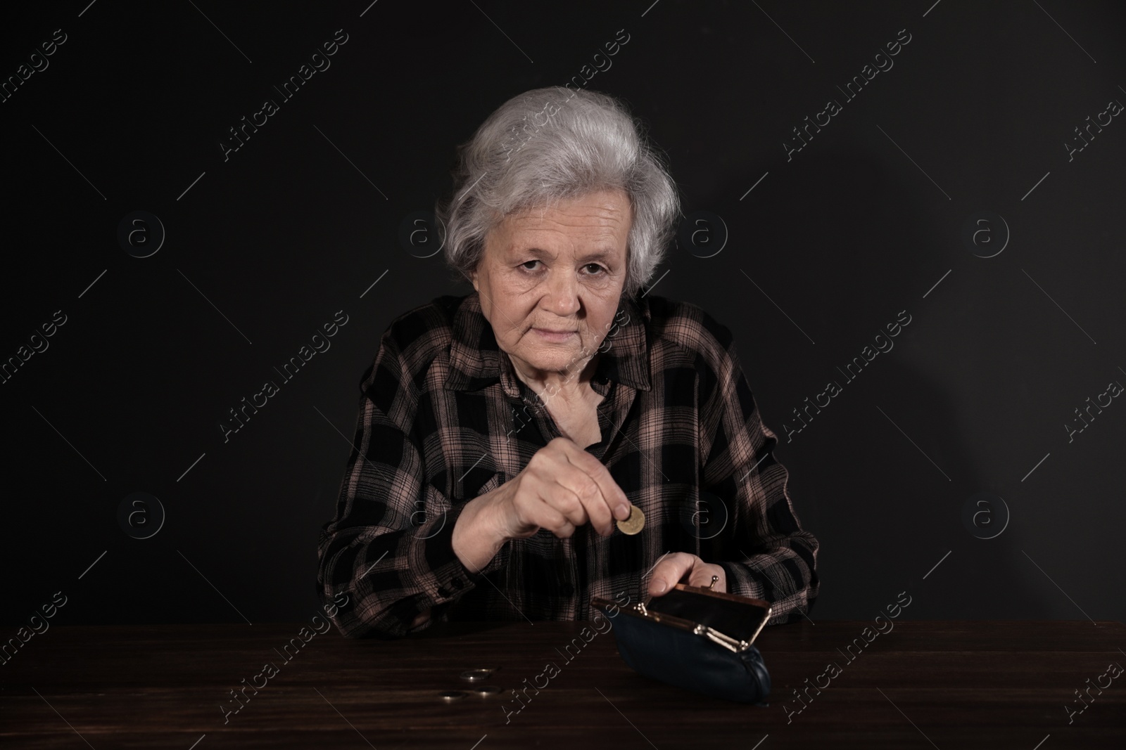 Photo of Poor mature woman putting coins into wallet at table