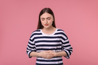 Photo of Young woman suffering from stomach pain on pink background