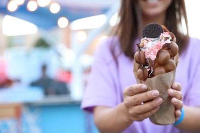 Photo of Young woman holding delicious sweet bubble waffle with ice cream outdoors, closeup