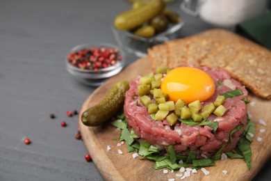 Photo of Tasty beef steak tartare served with yolk, pickled cucumber and other accompaniments on grey wooden table, space for text