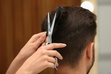 Barber making stylish haircut with professional scissors in beauty salon, closeup