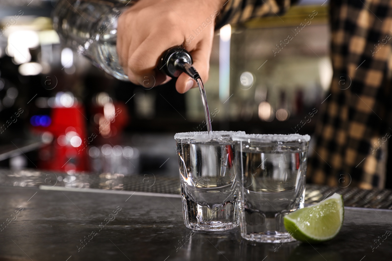 Photo of Bartender pouring Mexican Tequila into shot glasses at bar counter, closeup