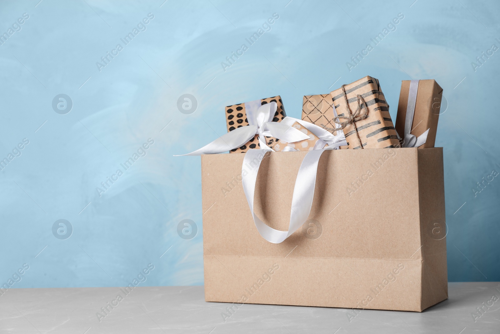 Photo of Paper shopping bag with handles full of gift boxes on table. Mock up for design