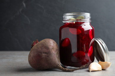 Pickled beets in glass jar on light table against dark background