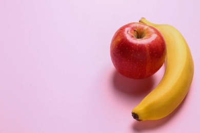 Tasty raw apple and banana on pink background, space for text