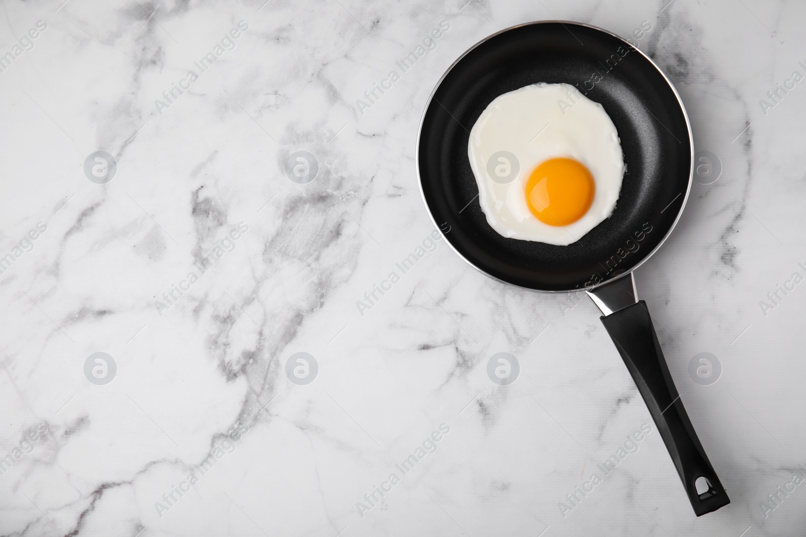 Photo of Tasty fried egg in pan on white marble table, top view. Space for text