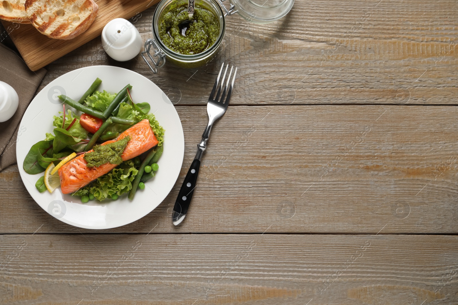 Photo of Tasty cooked salmon with pesto sauce served on wooden table, flat lay. Space for text