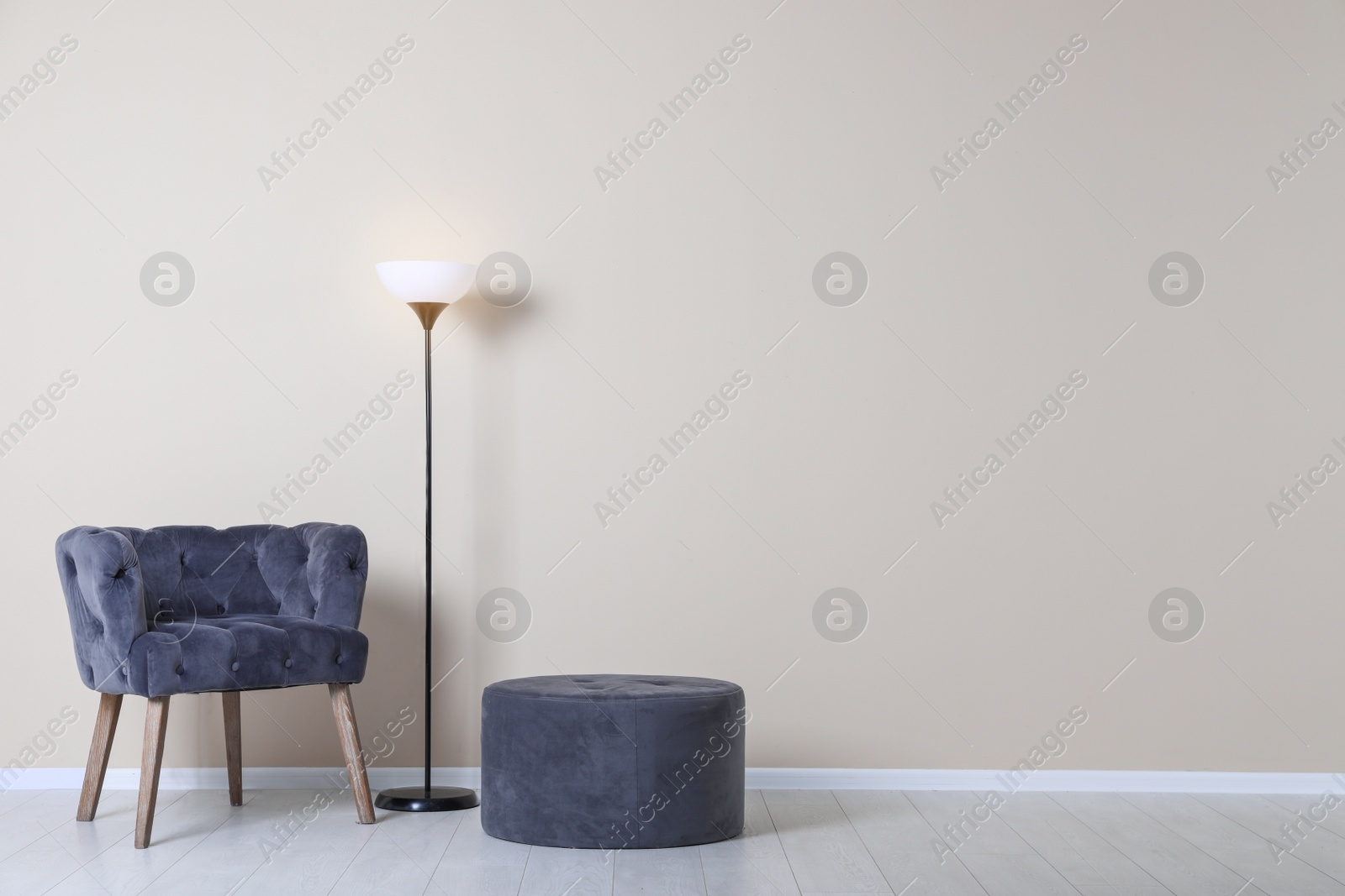 Photo of Comfortable armchair, pouf and lamp near color wall with space for text. Interior element