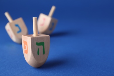 Photo of Hanukkah traditional dreidel with letters Pe and He on blue background, space for text