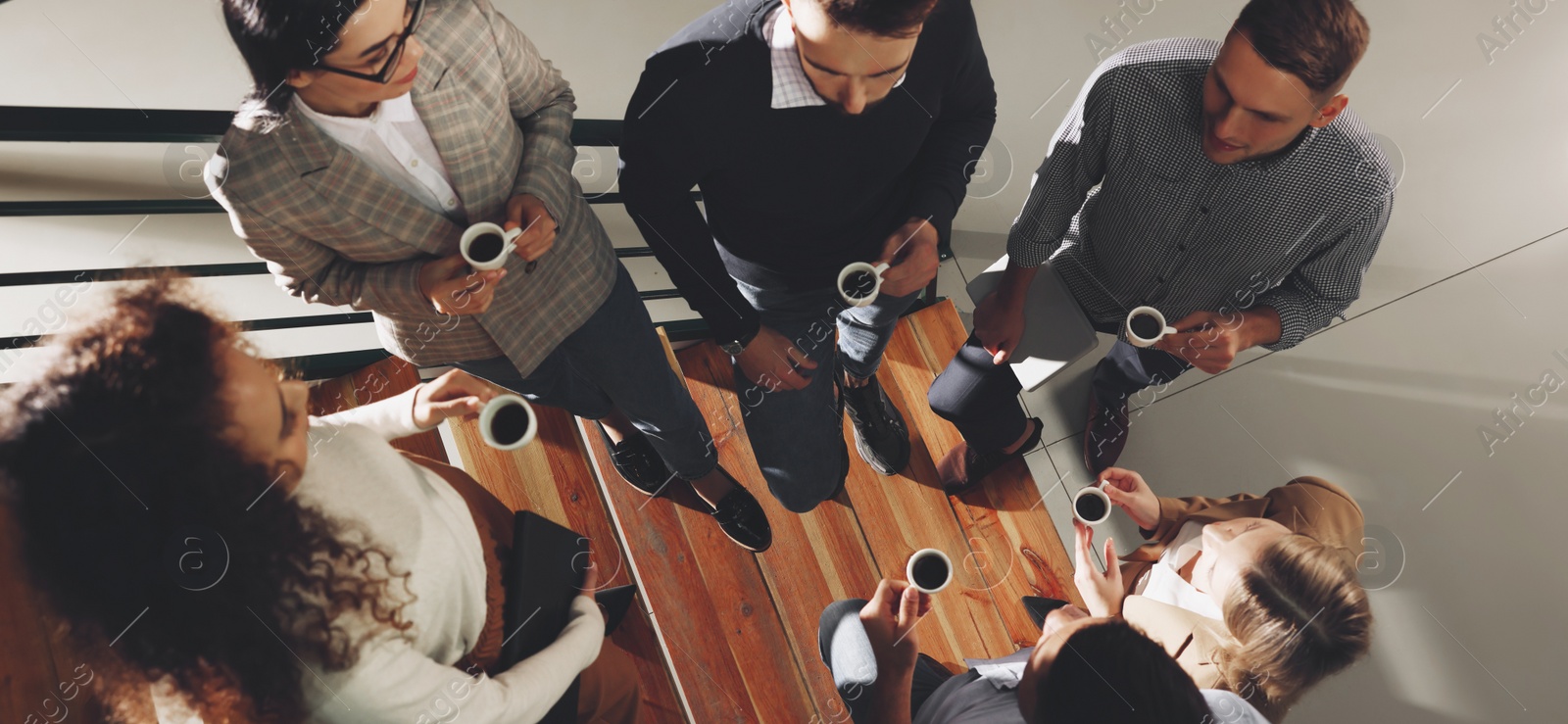 Image of Group of coworkers talking during coffee break on stairs in office, top view. Banner design