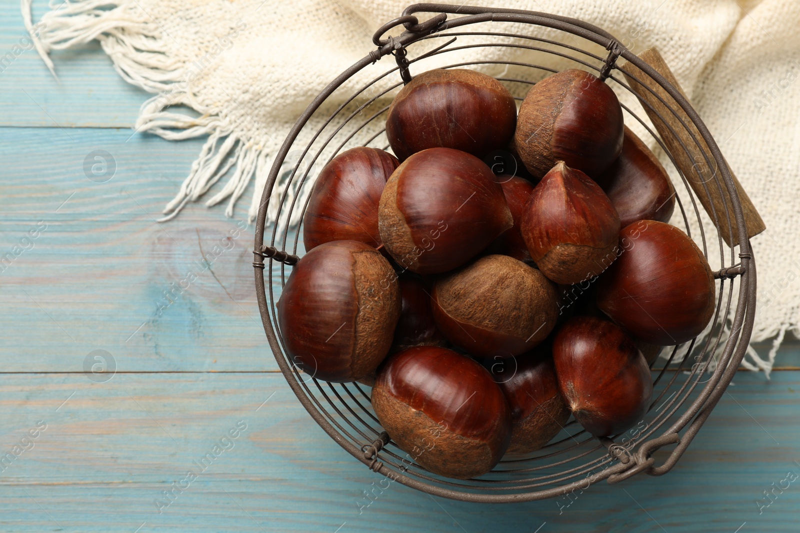 Photo of Roasted edible sweet chestnuts in metal basket on light blue wooden table, top view. Space for text