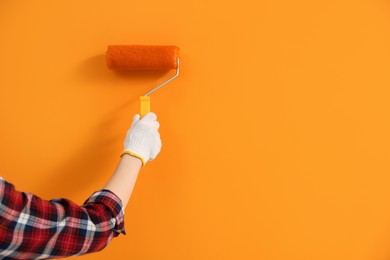 Photo of Designer painting orange wall with roller, closeup. Space for text