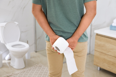 Photo of Man with toilet paper suffering from hemorrhoid in rest room, closeup