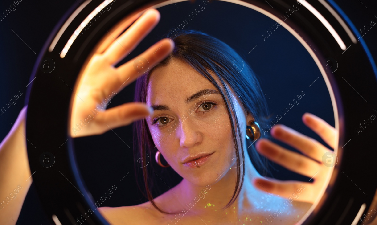 Photo of Portrait of beautiful woman on dark background in neon lights, view through ring lamp