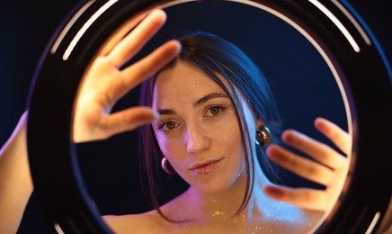 Photo of Portrait of beautiful woman on dark background in neon lights, view through ring lamp