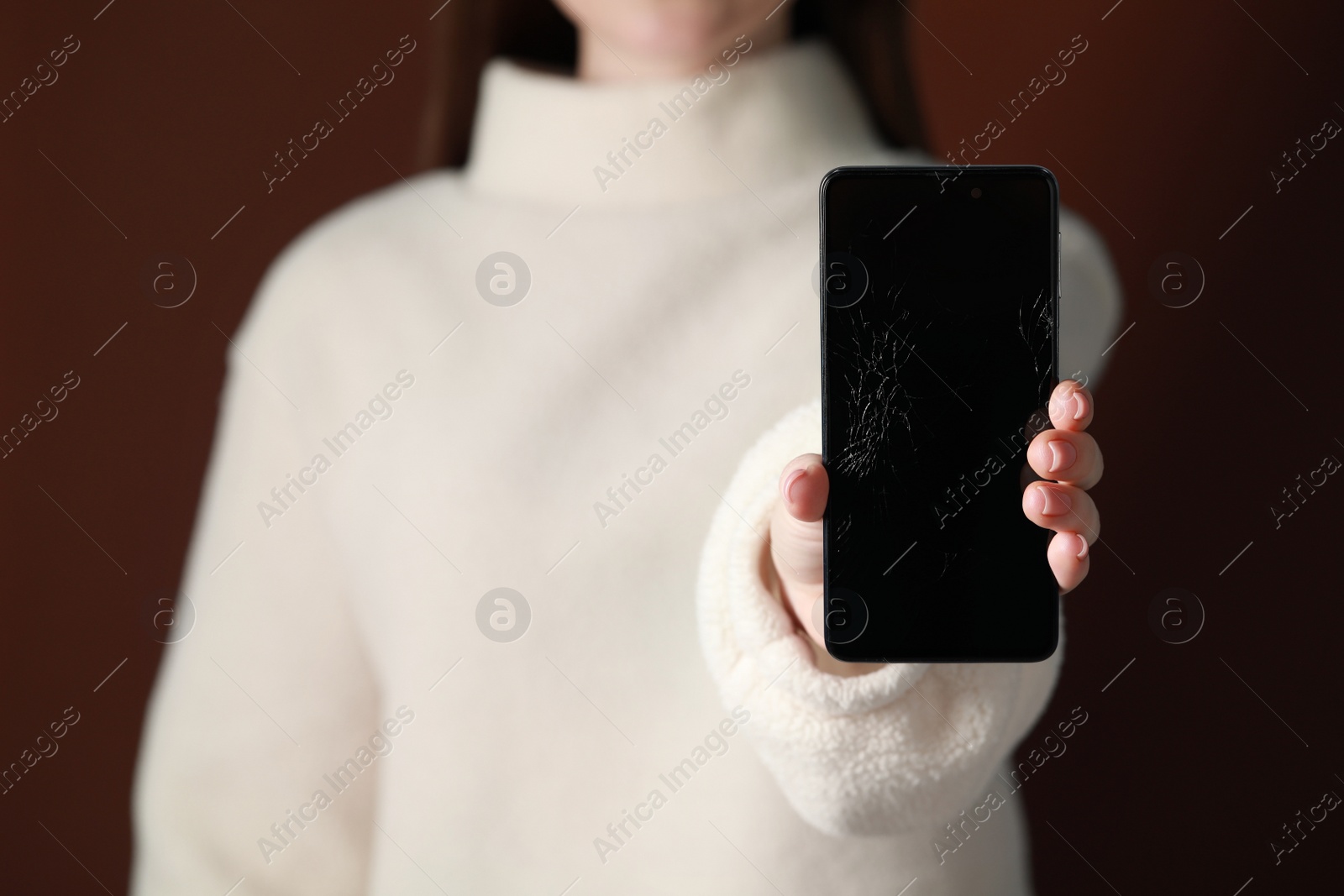 Photo of Woman showing damaged smartphone against brown background, closeup. Device repairing