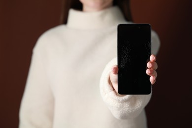 Photo of Woman showing damaged smartphone against brown background, closeup. Device repairing