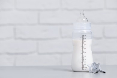 Feeding bottle with infant formula and pacifier on light grey table against brick wall. Space for text