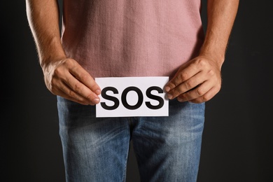 Man holding SOS sign on black background, closeup. Urology problems