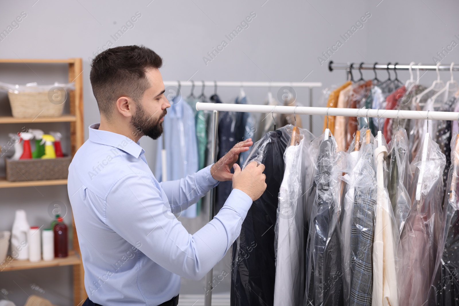 Photo of Dry-cleaning service. Worker choosing clothes from rack indoors