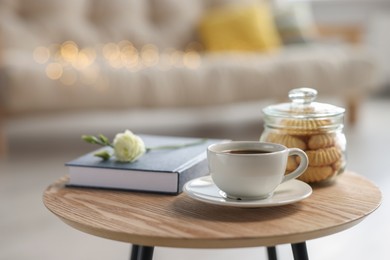 Photo of Cup of coffee, cookies, book and eustoma flower on wooden table in living room