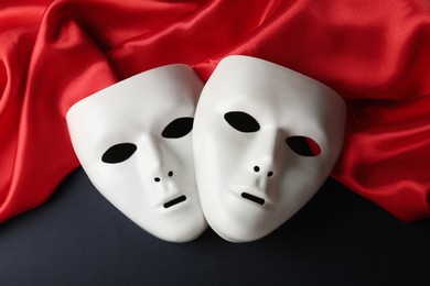 Photo of White theatre masks and red fabric on black background, flat lay