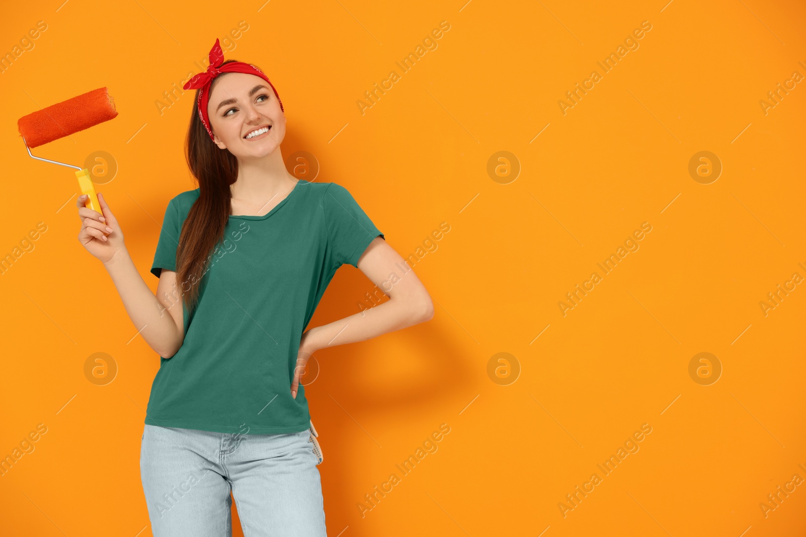Photo of Happy designer with roller near freshly painted orange wall, space for text