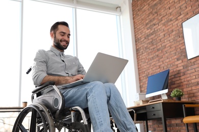Photo of Young man in wheelchair using laptop at office