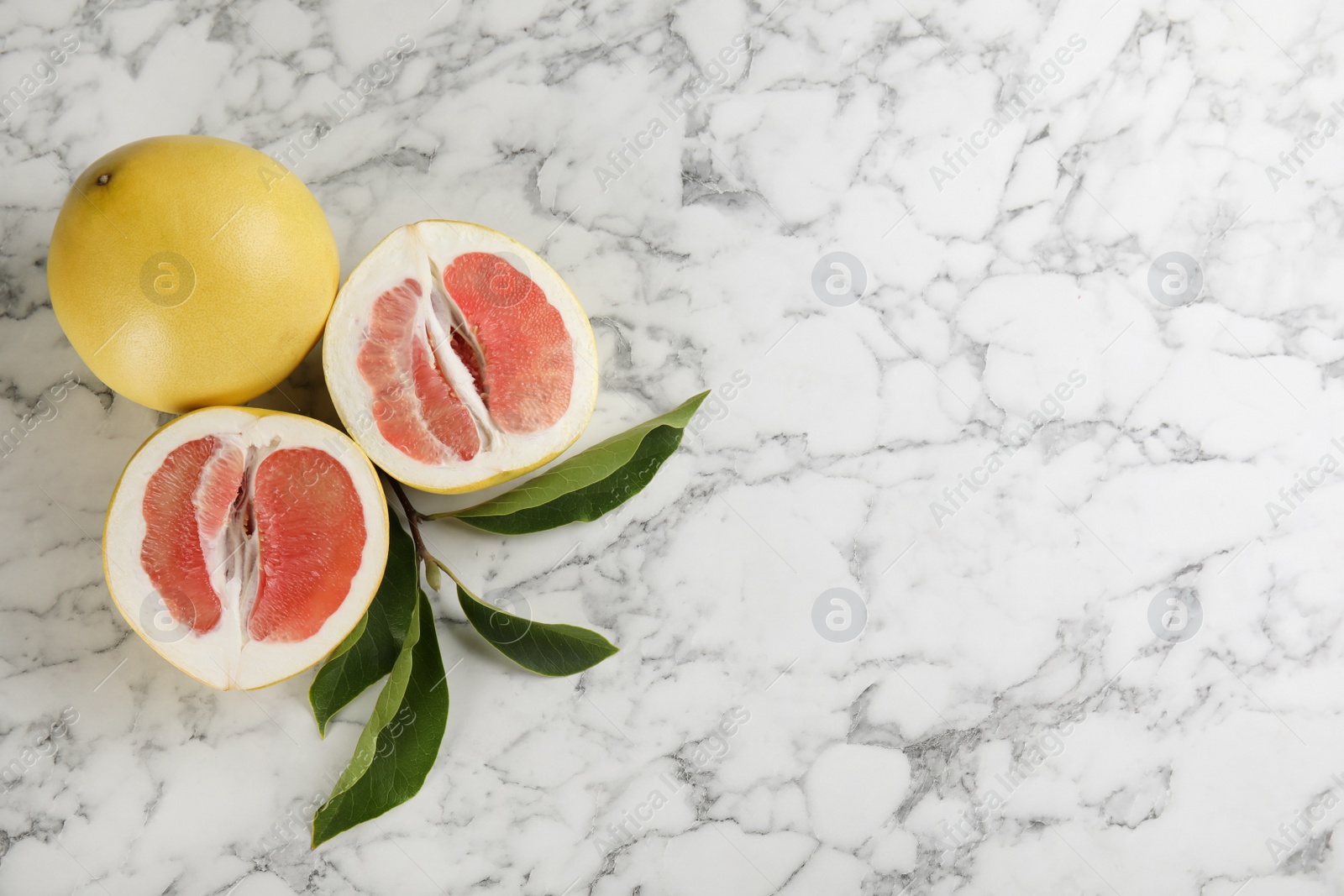 Photo of Fresh cut and whole pomelo fruits on white marble table, flat lay. Space for text