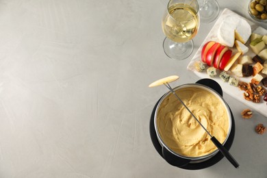 Photo of Fork with piece of apple, melted cheese in fondue pot and snacks on grey table, flat lay. Space for text