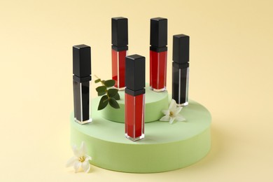 Photo of Different lip glosses, podiums and flowers on beige background