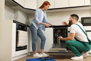 Young woman discussing with repairman near dishwasher in kitchen, low angle view