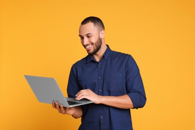 Photo of Smiling young man working with laptop on yellow background