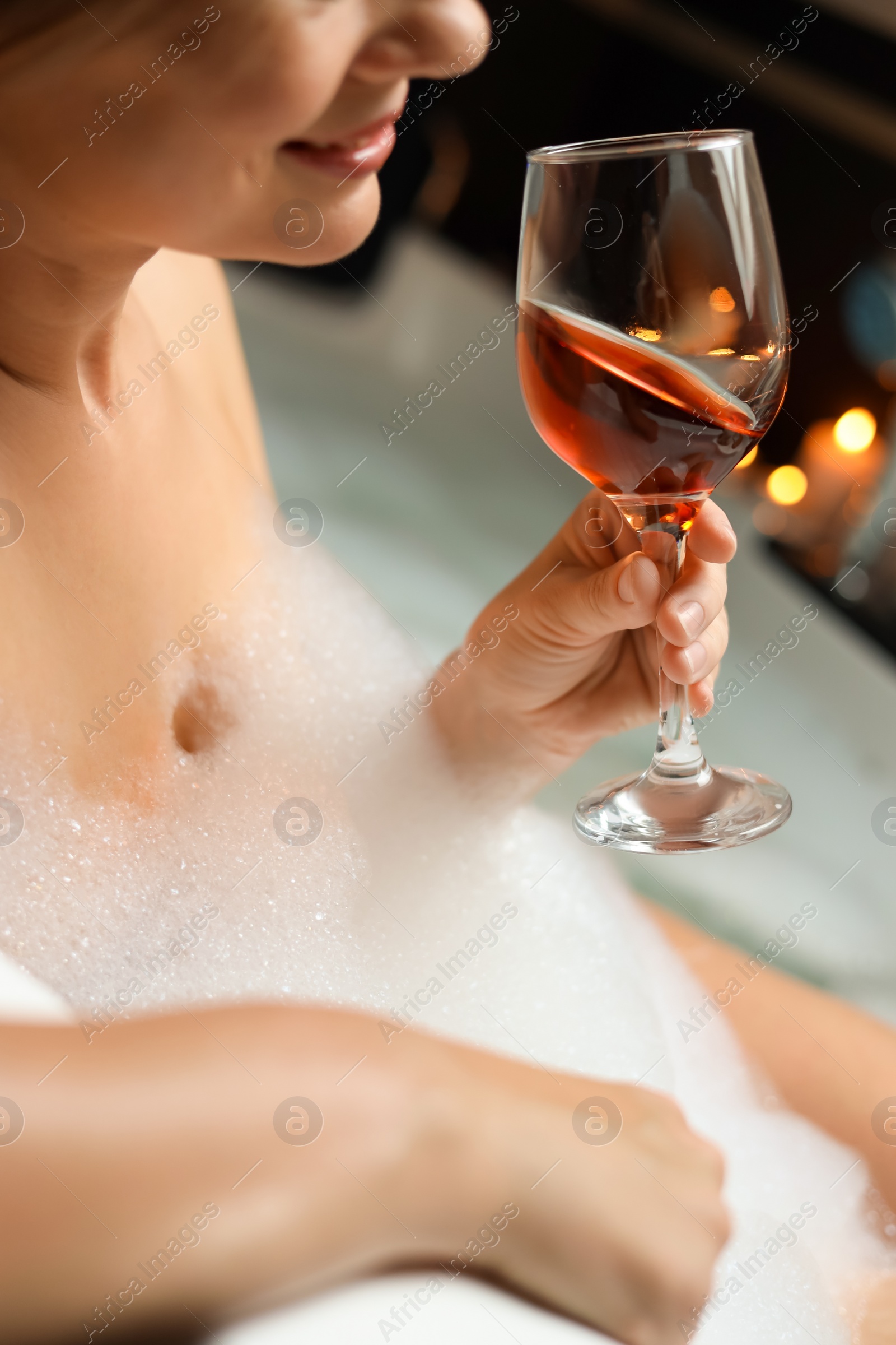 Photo of Woman drinking wine while taking bubble bath, closeup. Romantic atmosphere