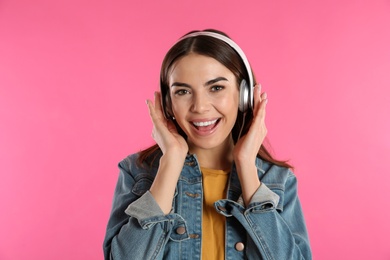 Beautiful young woman listening to music with headphones on color background