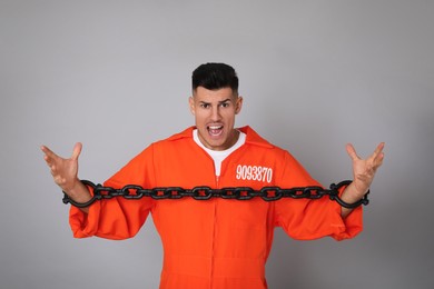 Emotional prisoner in orange jumpsuit with chained hands on grey background