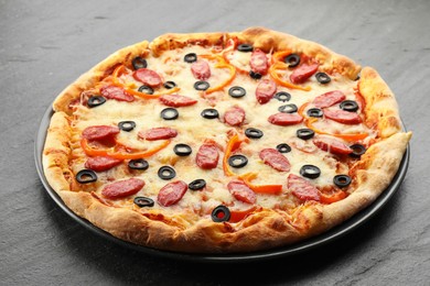 Photo of Tasty pizza with cheese, dry smoked sausages, olives and pepper on grey table