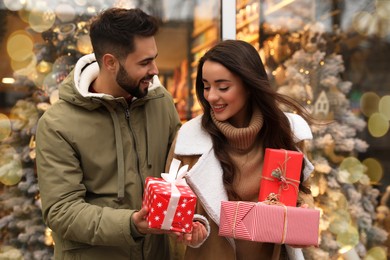 Photo of Lovely couple with presents near store decorated for Christmas outdoors