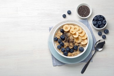 Photo of Tasty oatmeal with banana, blueberries and chia seeds served in bowl on white wooden table, flat lay. Space for text