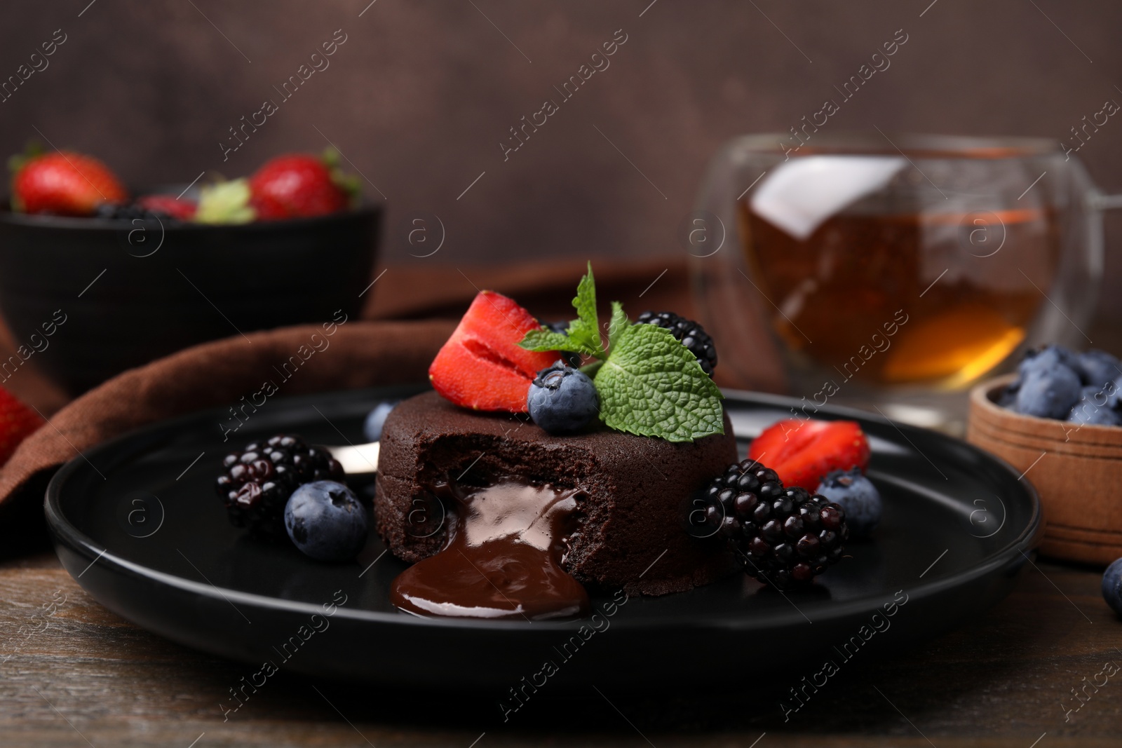 Photo of Plate with delicious chocolate fondant, berries and mint on wooden table, closeup