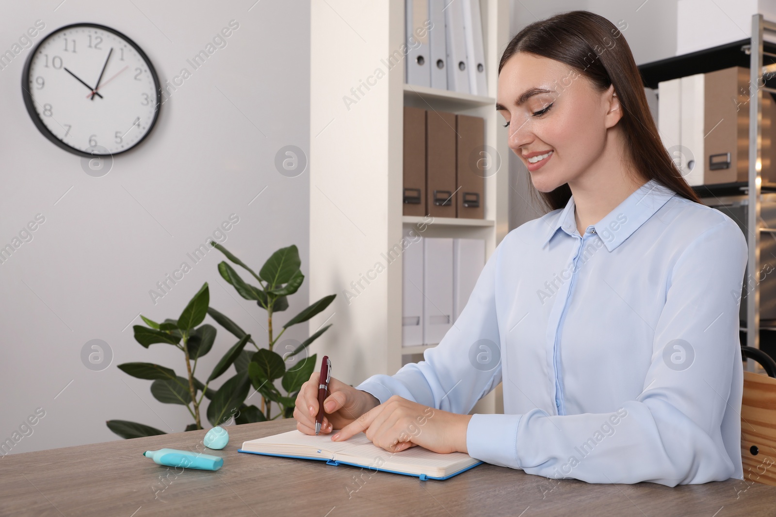 Photo of Happy woman taking notes at wooden table in office, space for text