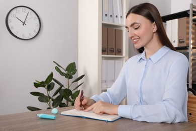 Photo of Happy woman taking notes at wooden table in office, space for text