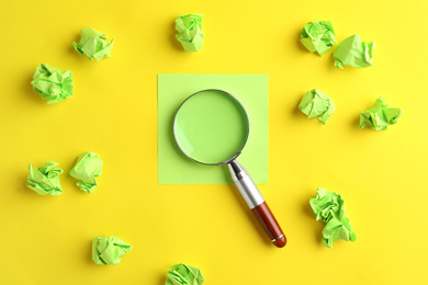 Photo of Magnifier glass, empty card and green crumpled paper sheets on yellow background, flat lay. Find keywords concept