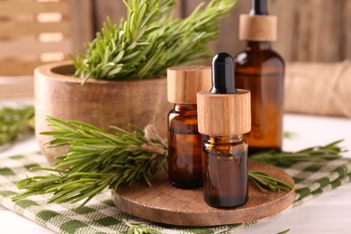 Essential oil in bottles and rosemary on white wooden table, closeup