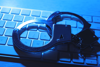Handcuffs and computer keyboard on table, closeup. Cyber crime