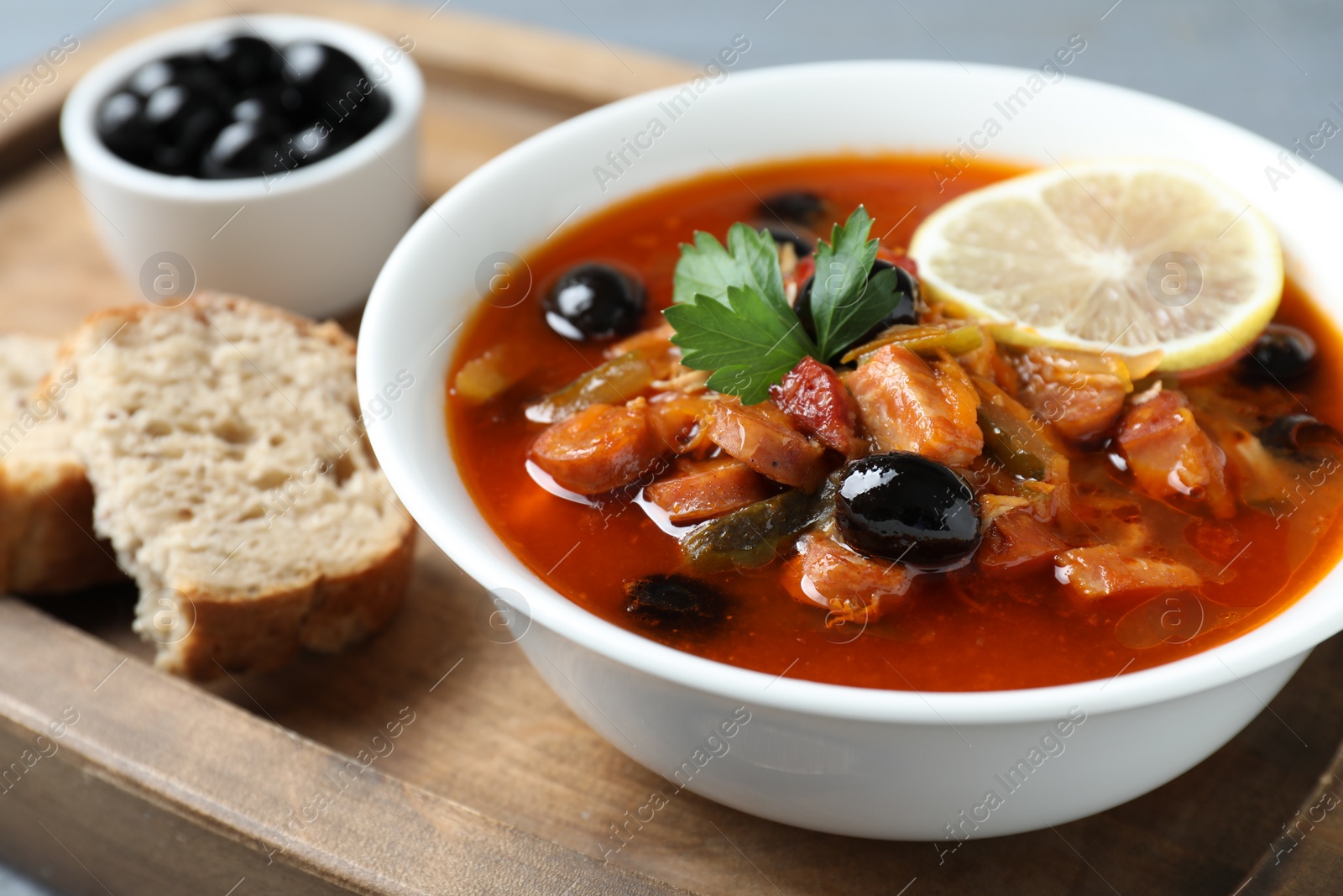 Photo of Meat solyanka soup with sausages, olives and vegetables in bowl served on table, closeup