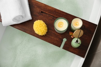 Photo of Wooden bath tray with candles, air freshener, towels and sponge on tub, top view